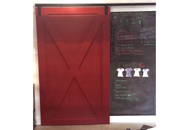 Red x-frame barn door with black track next to chalkboard 